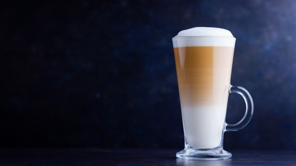 Latte macchiato in a tall glass on a dark background. Cafe latte layered with milk in a high drinking glass. Minimalism. Сopy space