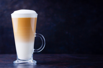 Latte macchiato in a tall glass on a dark background. Cafe latte layered with milk in a high drinking glass. Minimalism. Сopy space