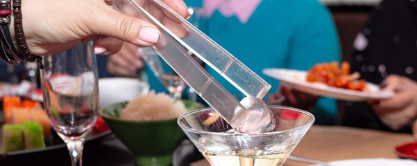 Woman hand adds an ice cube to vermouth cocktail at a holiday dinner - obrazy, fototapety, plakaty