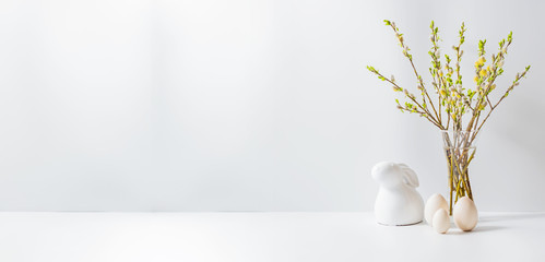 Home interior with easter decor. Willow branches in a glass vase, easter eggs on a light background