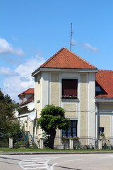 Renovated attached suburban family house with tower like corner covered with new facade and roof tiles surrounded with metal fence and trees next to paved road on clear blue sky background
