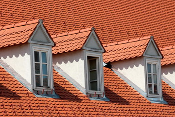 Row of renovated old style roof windows covered with new red roof tiles and snow guards on top of suburban family house in old part of town