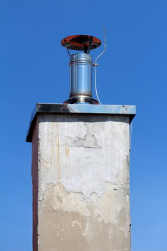 Shiny metal new small chimney with metal cap and lightning rod on top of dilapidated concrete foundation with cracked facade on clear blue sky background