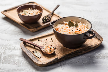 Fermented cabbage in a plate on a wooden tray with a spoon on a light background.