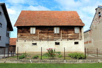 Vintage rustic retro old wooden suburban family house with tall concrete foundation and narrow windows surrounded with other houses and small flower and vegetables garden in front on cloudy blue sky b