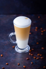 Latte macchiato in a tall glass. Glass of coffee latte and coffee beans on a dark background. Minimalism. Сopy space