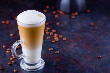 Latte macchiato in a tall glass. Glass of coffee latte and coffee beans on a dark background. Minimalism. Сopy space