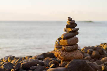 Balanced stone pyramide on shore of the ocean at dawn. Sea pebbles tower closeup symbolizing stability, zen, harmony, balance.