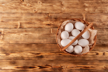 Farm eggs in a wicker basket on a wooden table. Copy space, top view.
