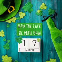 St Patrick Day dark green wooden rustic background with shamrocks and leprechaun costume accessories, date march 17 on vintage wooden calendar. May the luck be with you text quote - 326137120