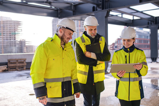 Group of engineers standing outdoors on construction site, using tablet.