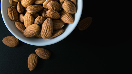 superfood concept, almonds in a white plate on a black table, top view