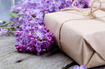 Handmade gift boxes wrapped with craft brown paper, decorated with fresh purple lilac flowers on a vintage wooden surface.