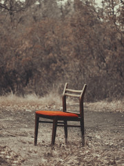 Fototapeta premium Bright red chair (Vertical). A bright red chair outside. Discarded furniture, old stuff. A chair from the trash can. Alone in the background of the forest. Bright red.