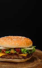 Big burger with beef buffet, cheese and herbs on a wooden tray in the form of a tree on a black background