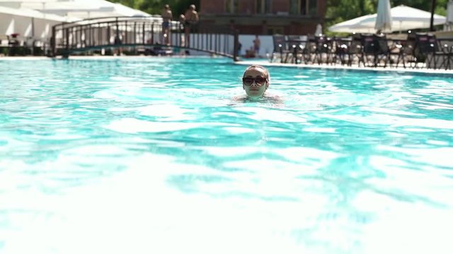 beautiful young woman in sunglasses swimming and comes up on pool edge by hands and joyfully looking at camera. woman Enjoying Summer Travel In Swimming Pool At Luxury hotel spa