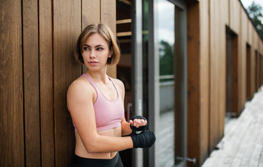 A young sportswoman standing outdoors on terrace, resting.
