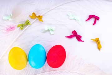 Easter composition with colored eggs feathers and bows on a white background.
