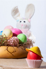Red egg in a white stand and hat on a background of a plate with eggs and a hare. Easter Composition.