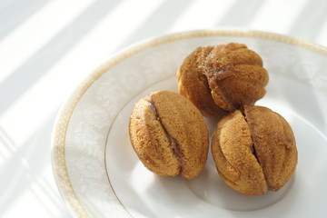 Three small cookies in the form of walnuts on a white saucer and a sunny table