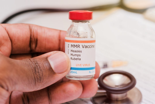 measles mumps and rubella vaccine concept african american doctor holding syringe in front of vaccination vial and stethoscope and clipboard with checklist