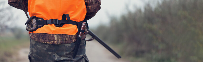 A man with a gun in his hands and an orange vest on a pheasant hunt in a wooded area in cloudy...