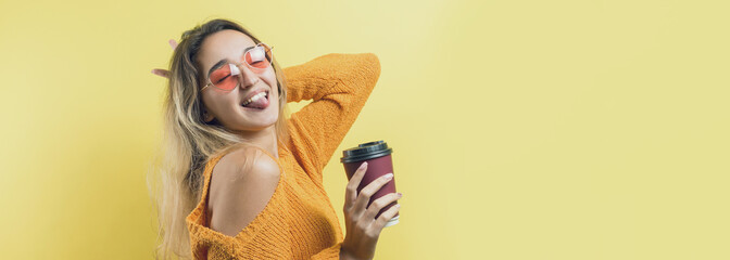 Glamor woman in glasses in an orange sweater with a drink of coffee on a yellow background..