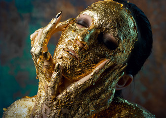 Girl with a mask on her face made of gold leaf. Gloomy studio portrait of a brunette on an abstract background.