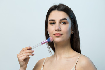 Close-up of a young girl in a light top on a white background making a facial make-up. A pretty...