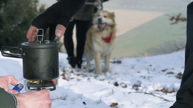 Portable Gas Stove Being Lit With Dog Walkers In The Background On Snow Covered Hill. Locked Off 