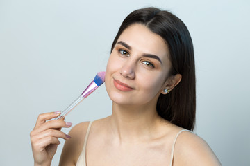 Close-up of a young girl in a light top on a white background making a facial make-up. A pretty...