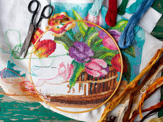 Cross stitch pattern of tulips, purple, blue, beige flowers on an old wooden natural background. Screensaver for the desktop. Needlework, handmade, hobbies, free time.