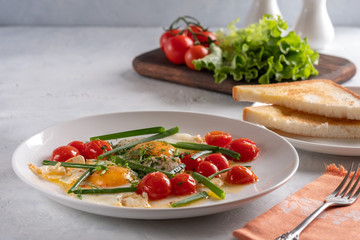 Fried eggs with cherry tomatoes and green onions on a white plate