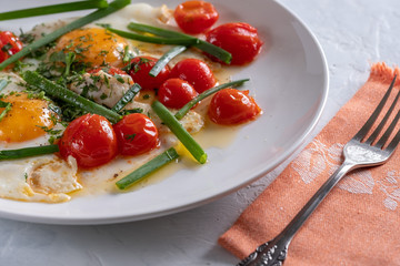 Fried eggs with cherry tomatoes and green onions on a white plate