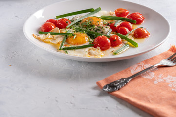 Fried eggs with cherry tomatoes and green onions on a white plate