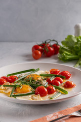Fried eggs with cherry tomatoes and green onions on a white plate
