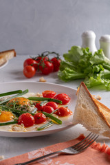 Fried eggs with cherry tomatoes and green onions on a white plate