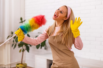 Beautiful housewife is singing while cleaning with duster her home.	