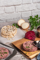 Raw veggie burger with beetroot and white beans with parsley leaves on wood cutting board.