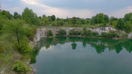 Fototapeta na wymiar Abandoned granite quarry filled with water and trees. Granite ledges career over the water in the middle of green trees and bushes. Spring day on an abandoned stone quarry.