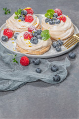 Mini pavlova meringue cakes with fresh raspberries and blueberries with mint leaves.