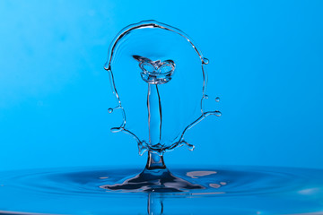 Naklejka na ściany i meble Abstract photograph of a water drop collision created with two water drops splashing together isolated against a blue background.