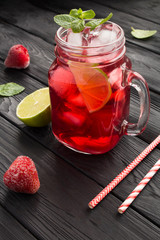 Cold lemonade with strawberries and lime on the black wooden  background. Location vertical. Closeup.