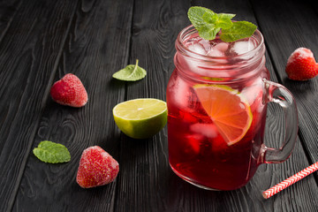 Cold lemonade with strawberries and lime on the black wooden  background. Closeup.