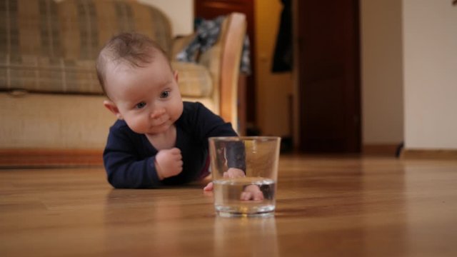 Toddler child awkwardly takes a glass of water and spills water on the floor at home