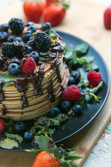 Sweet fresh pancakes with chocolate. Pancakes decorated with fresh raspberries, blueberries and blueberries, on a wooden Board on the kitchen table with a tablecloth. Delicious dessert.