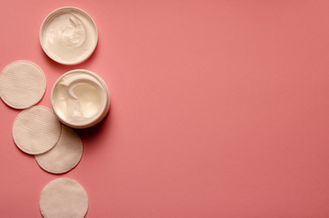 The Bank's with a white cream, napkins for face, the cover is open,on a pink background,cosmetology, beauty and skin care.