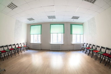 Fototapeta premium Large hall with three windows interior. Chairs along two sides, hardwood floor, beige walls and green curtains.