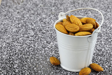 A white metal bucket filled with almond nuts stands on black and white marble