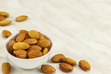 Almond nuts lie in a white bowl and on a white marble surface